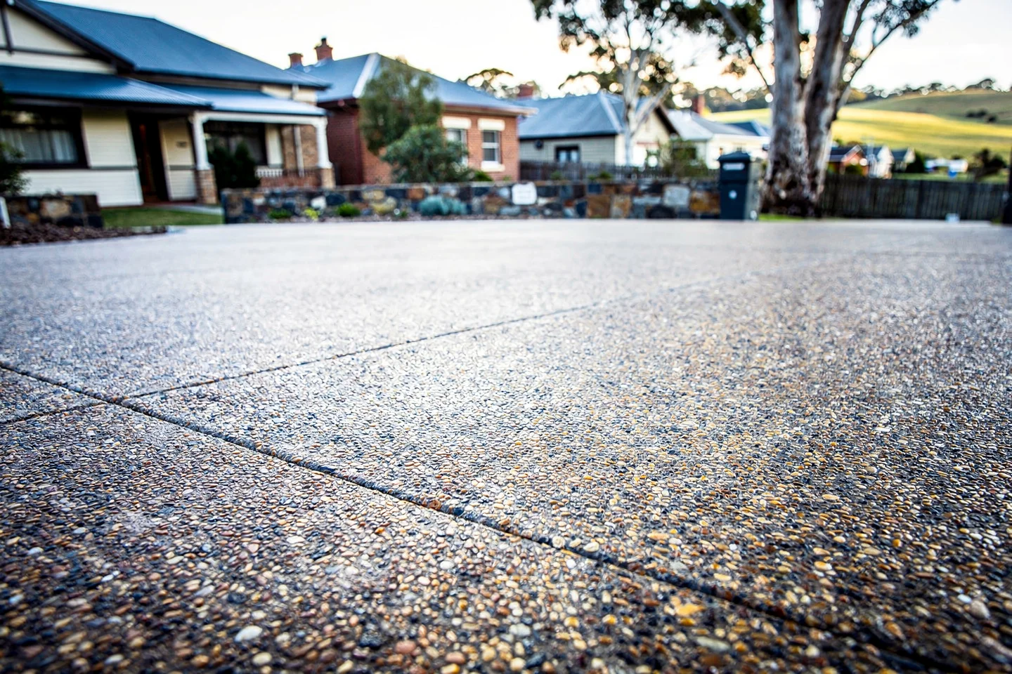 A finished exposed-aggregate slab surface with basalt-and-honey stone and a clean sawcut control joint